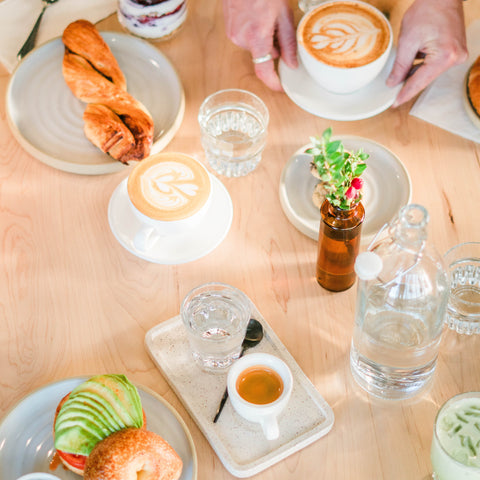 Table setting with coffee, pastries, and small dishes on a wooden table.